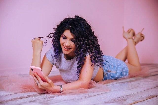 A woman lying down with a phone in her hand and smiling to herself.